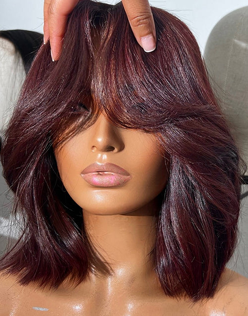 Close-up view of hands styling the face-framing curtain bangs on a 99J burgundy red wavy short blunt cut bob wig, demonstrating the natural hair movement and texture.