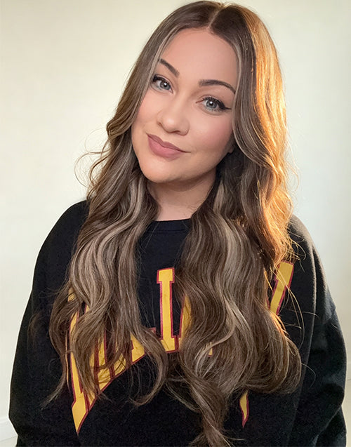 Woman wearing long wavy lace wig with center part, blonde highlights framing the face, and seamless scalp integration.