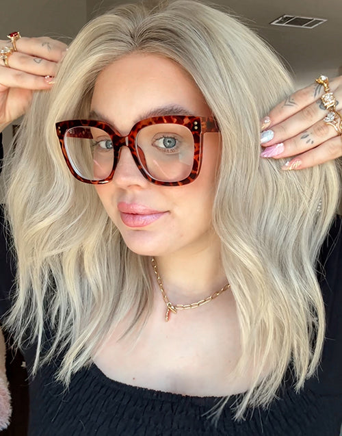 A model wearing an ombre ash blonde wavy human hair glueless bob wig, featuring tortoise shell glasses and stylish accessories.